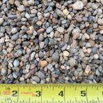 1/4″-3/8″ Pea Rock: small rounded pebbles in gray, tan and rust tones beside a tape measure